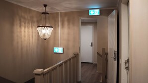 A hallway with a chandelier, an exit sign, and a door. - SteneBo Vandrarhem (Kågeröd)