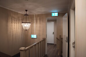 A hallway with a chandelier, an exit sign, and a door. - SteneBo Vandrarhem (Kågeröd)