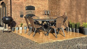 An outdoor patio with a brick wall, a table with chairs, a grill, and potted plants. - SteneBo Vandrarhem (Kågeröd)