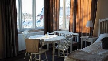 A hotel room with a bed, a small table with chairs, a lamp, and a view of the outside.
