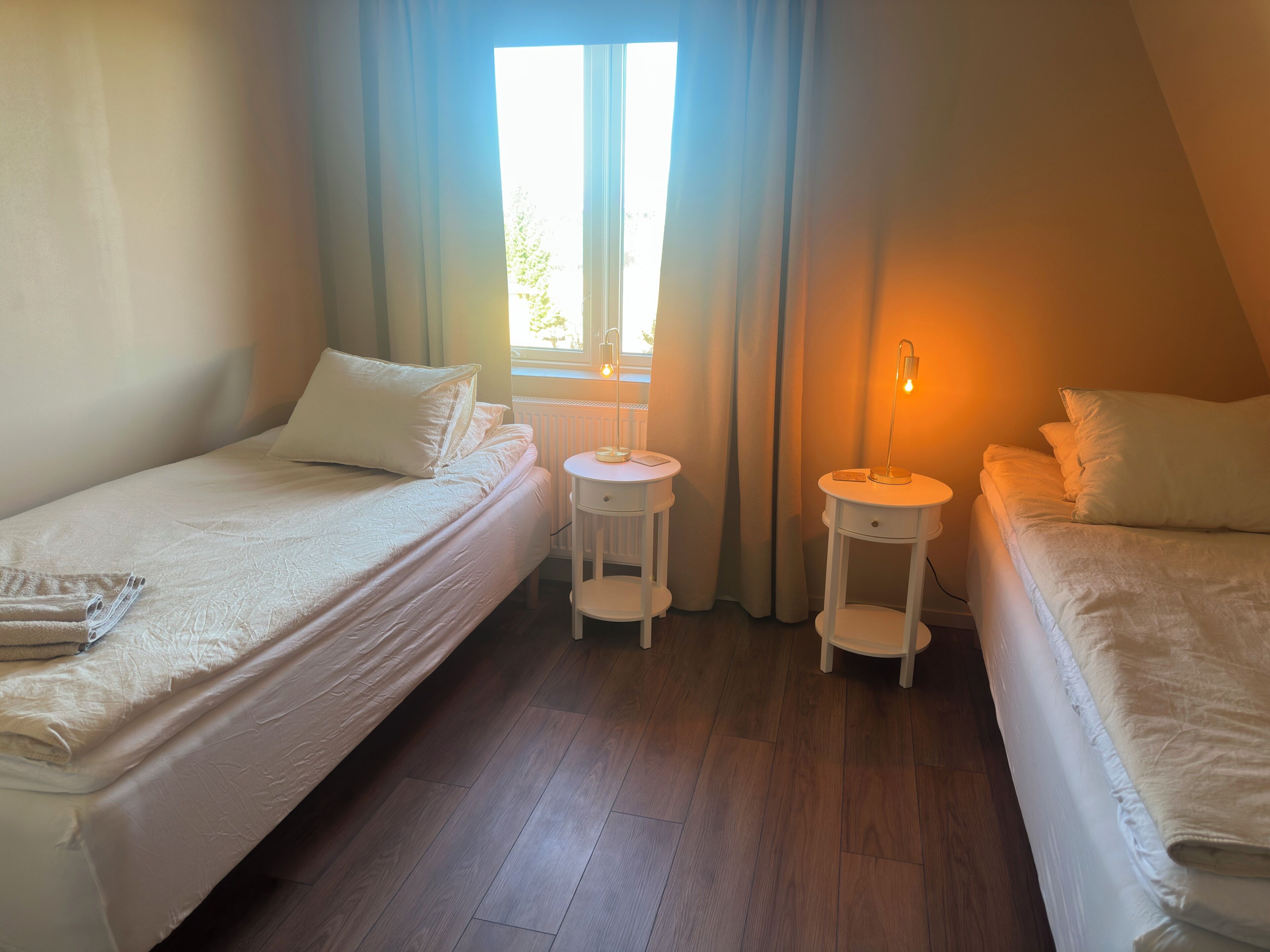 Een kamer met twee bedden, een raam en een nachtkastje met een lamp.