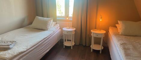 Een kamer met twee bedden, een raam en een nachtkastje met een lamp.