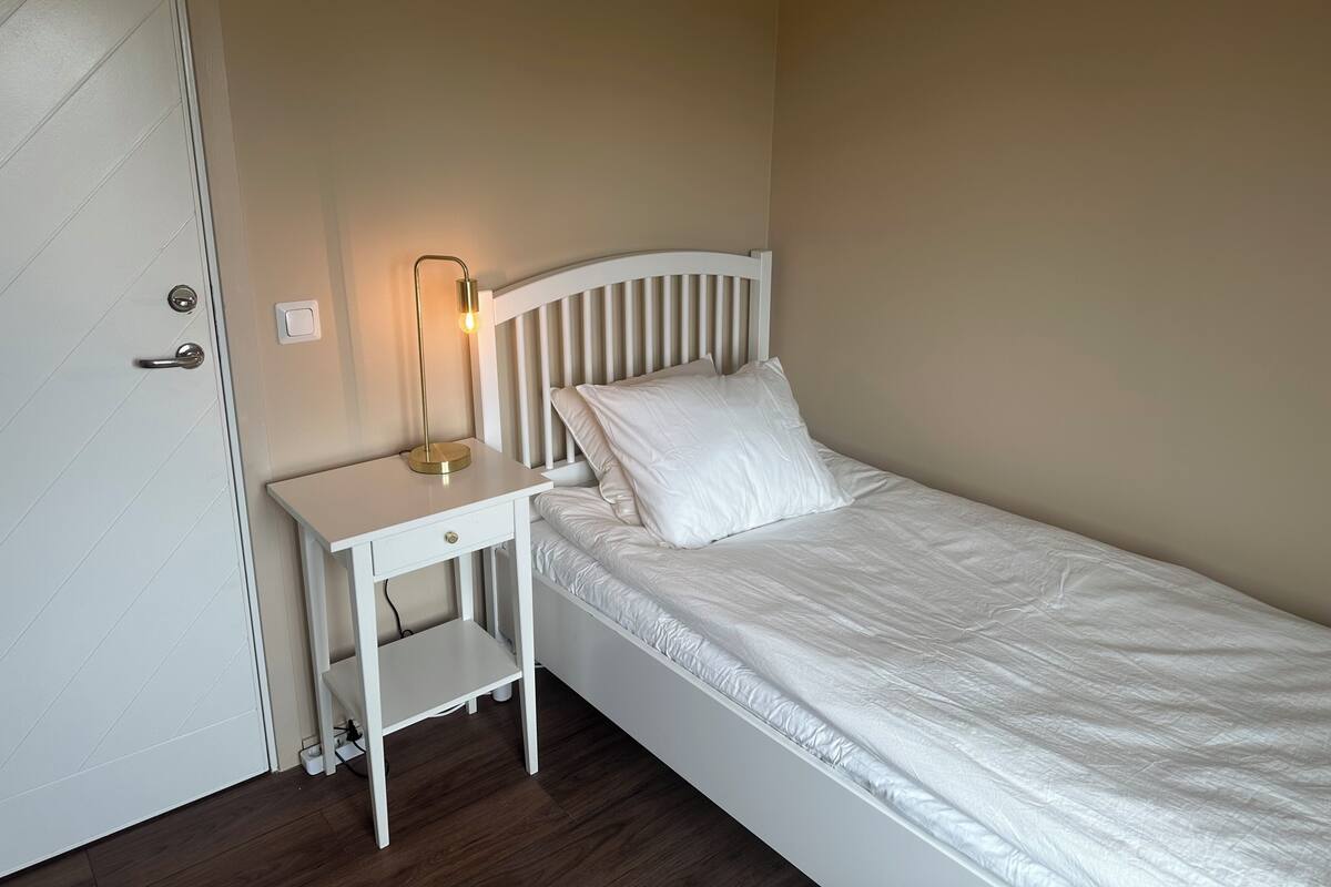 A single bed with a white headboard, a bedside table with a lamp, and a door with a handle.