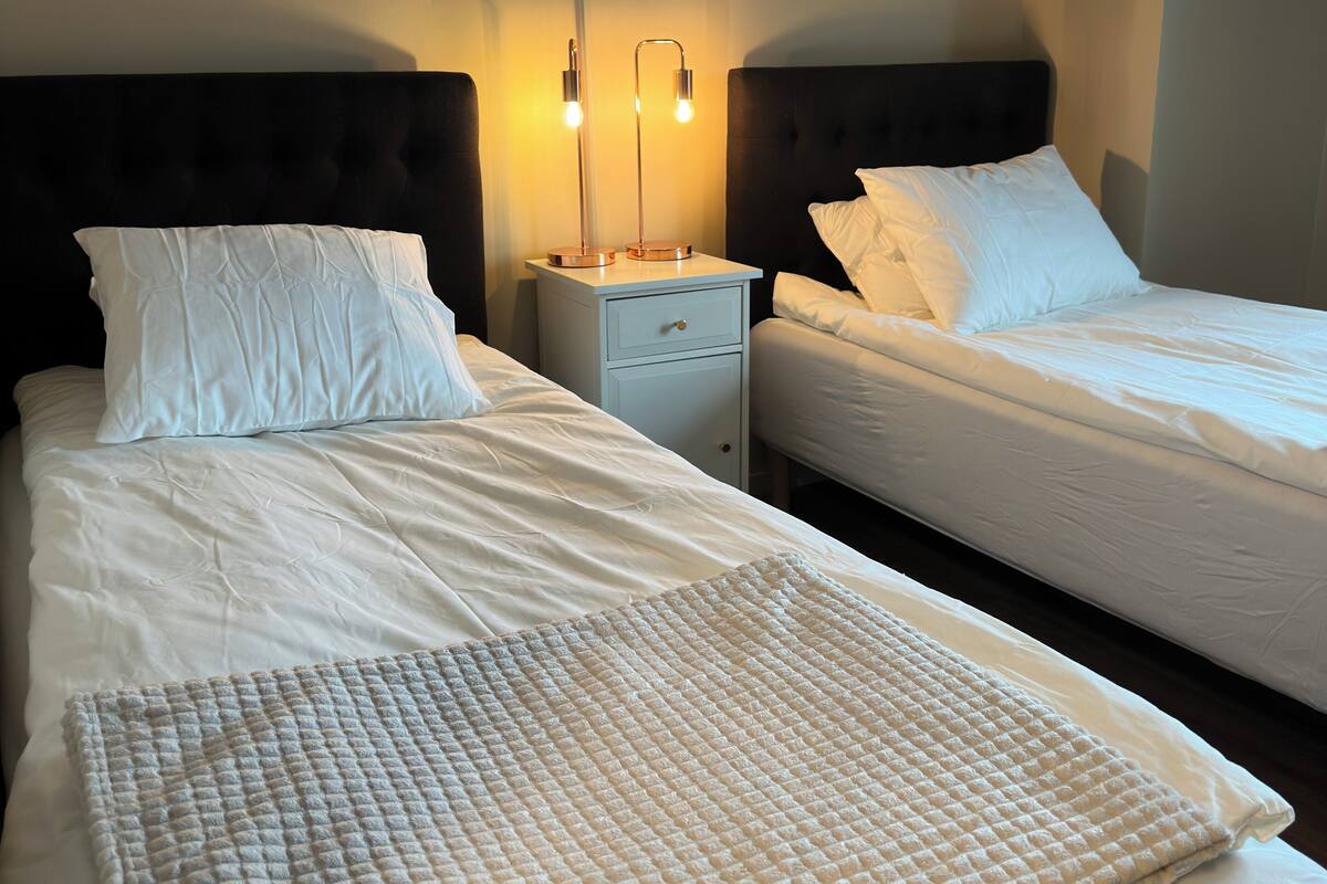 A hotel room with two beds, a nightstand with a lamp, and a quilted throw blanket.