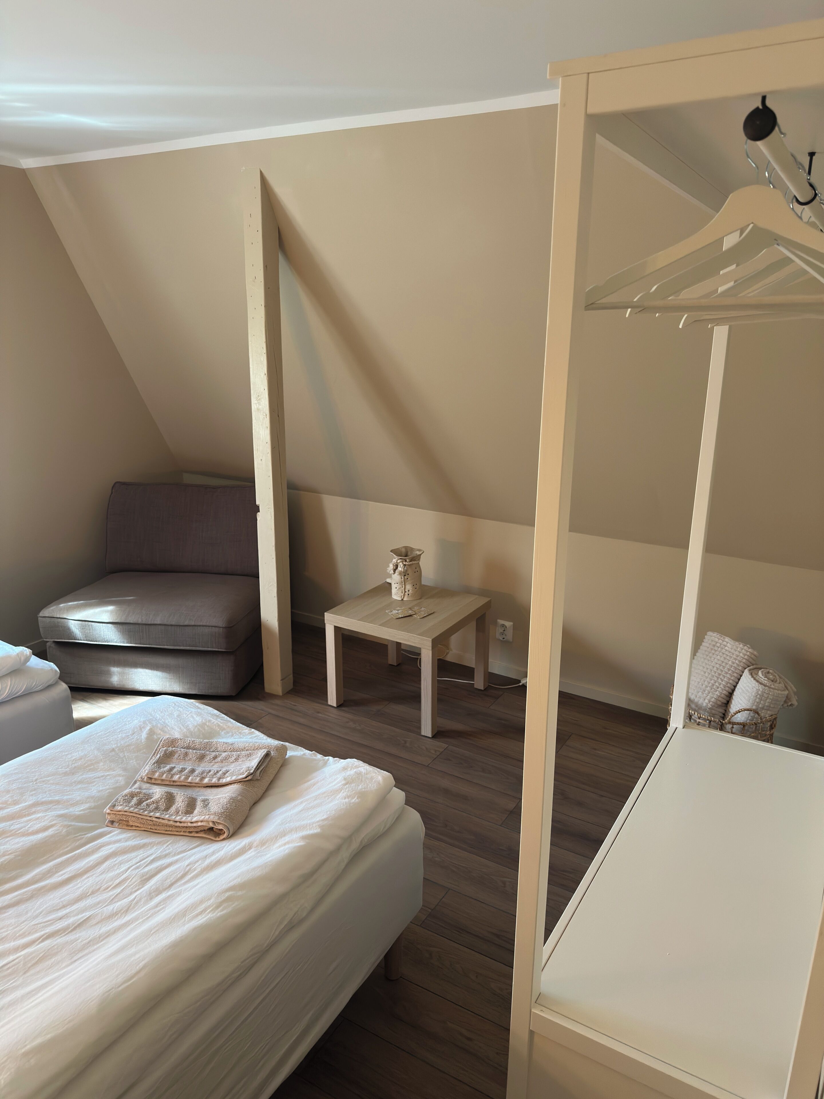 Een slaapkamer met een bed, een stoel, een klein tafeltje en een hangende lamp.