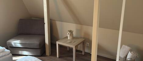 Un dormitorio con cama, una silla, una mesita y una lámpara colgante.