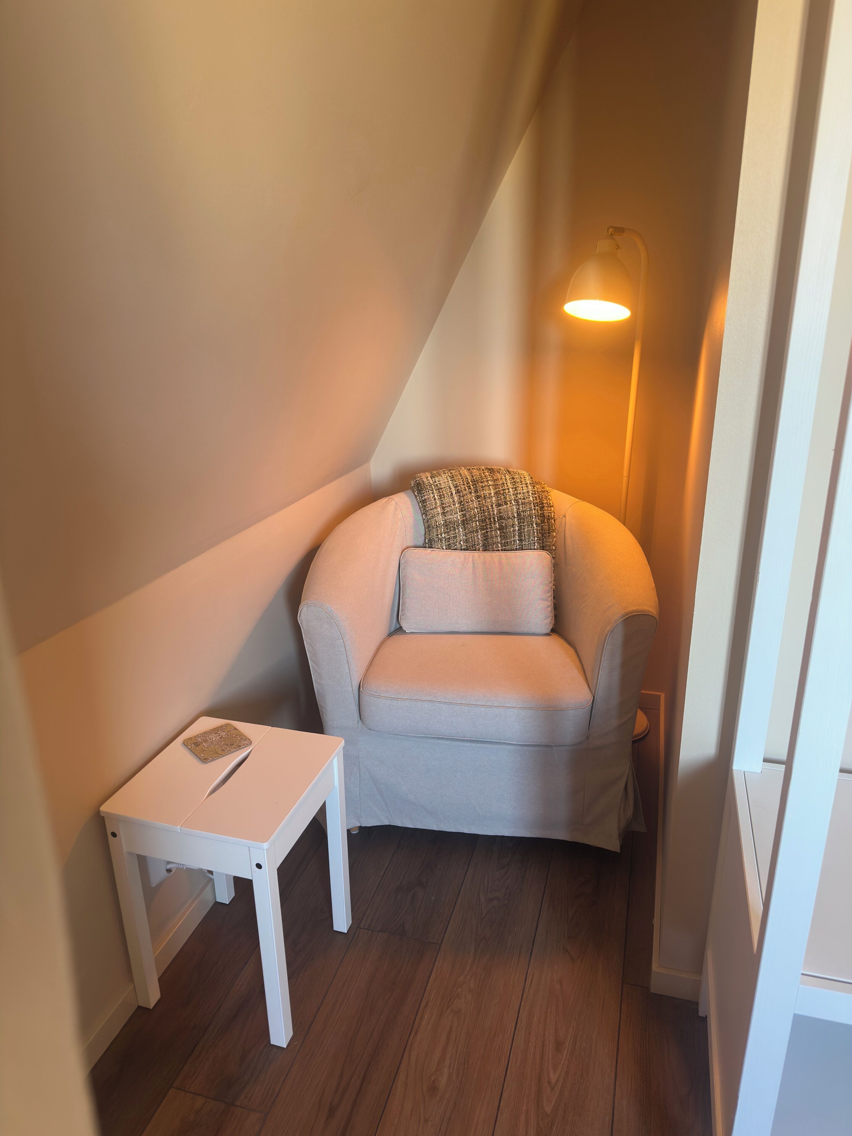 A small, cozy room with a light-colored sofa, a small table, and a wall-mounted lamp.