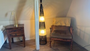 A room with a wooden floor, a desk with drawers, a chair with a towel, and a floor lamp. - SteneBo Vandrarhem (Kågeröd)