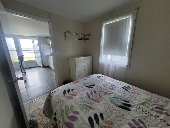 A bedroom with a bed, a dresser, a window with sheer curtains, and a door leading to a balcony.