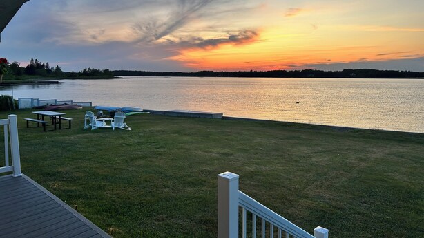 Terraza junto al lago con mesas y sillas de picnic, con vista a un lago tranquilo al atardecer.