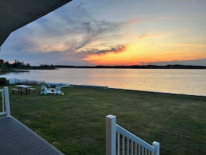 A lakeside deck with picnic tables and chairs, overlooking a calm lake during sunset.