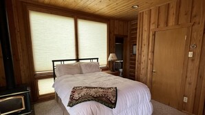 Ein Schlafzimmer einer Holzblockhütte mit einem Bett, einem Heizgerät und einem Fenster mit Jalousien.