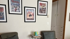 Ein Zimmer mit zwei Sesseln, einem kleinen Beistelltisch und einer Wand mit gerahmten Postern.