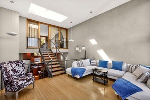 Un salon moderne avec un canapé, un fauteuil à motifs, un escalier et un coin repas.