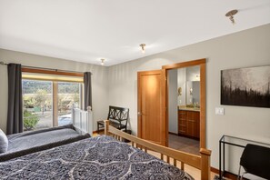 A bedroom with a large bed, a wooden door, a view of the outside, and a bathroom visible through a glass door.
