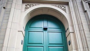 A green double door with a central panel and two side panels, set within an arched stone frame.