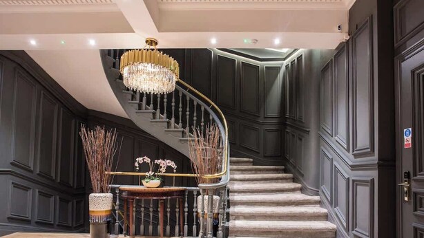 A grand staircase with a chandelier, dark wood paneling, and a small table with flowers. - Stylish City Escape | Walk to Chinatown | AC inc. (Greater Manchester)