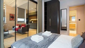 A modern hotel room with a large bed, a dark wardrobe, and a glass partition separating the bedroom from the living area. - Stylish City Escape | Walk to Chinatown | AC inc. (Greater Manchester)