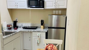 Cocina compacta con armarios blancos, un refrigerador de acero inoxidable, un microondas y una cafetera.