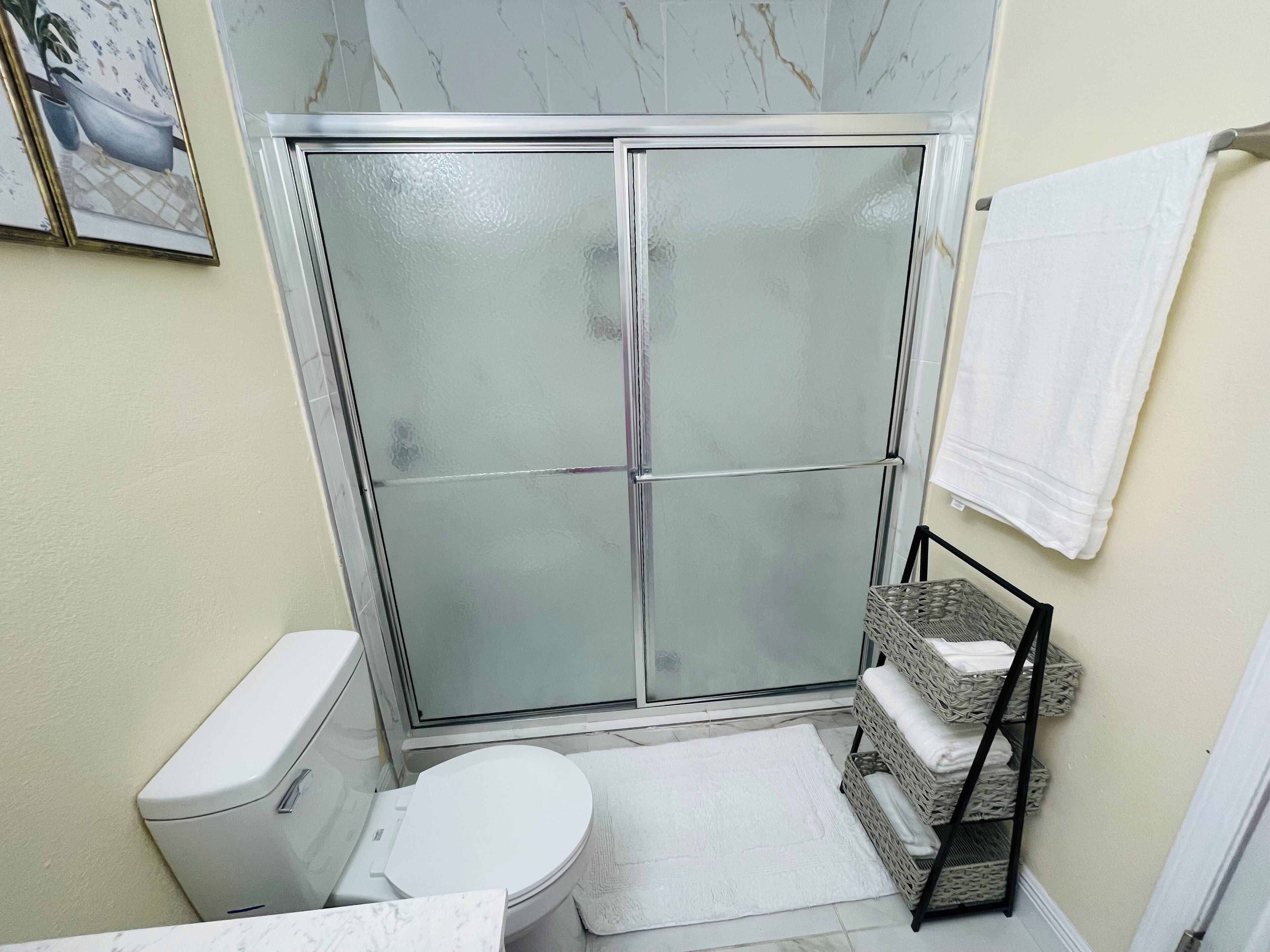 A compact bathroom with a glass shower enclosure, a toilet, and a small wicker shelf.