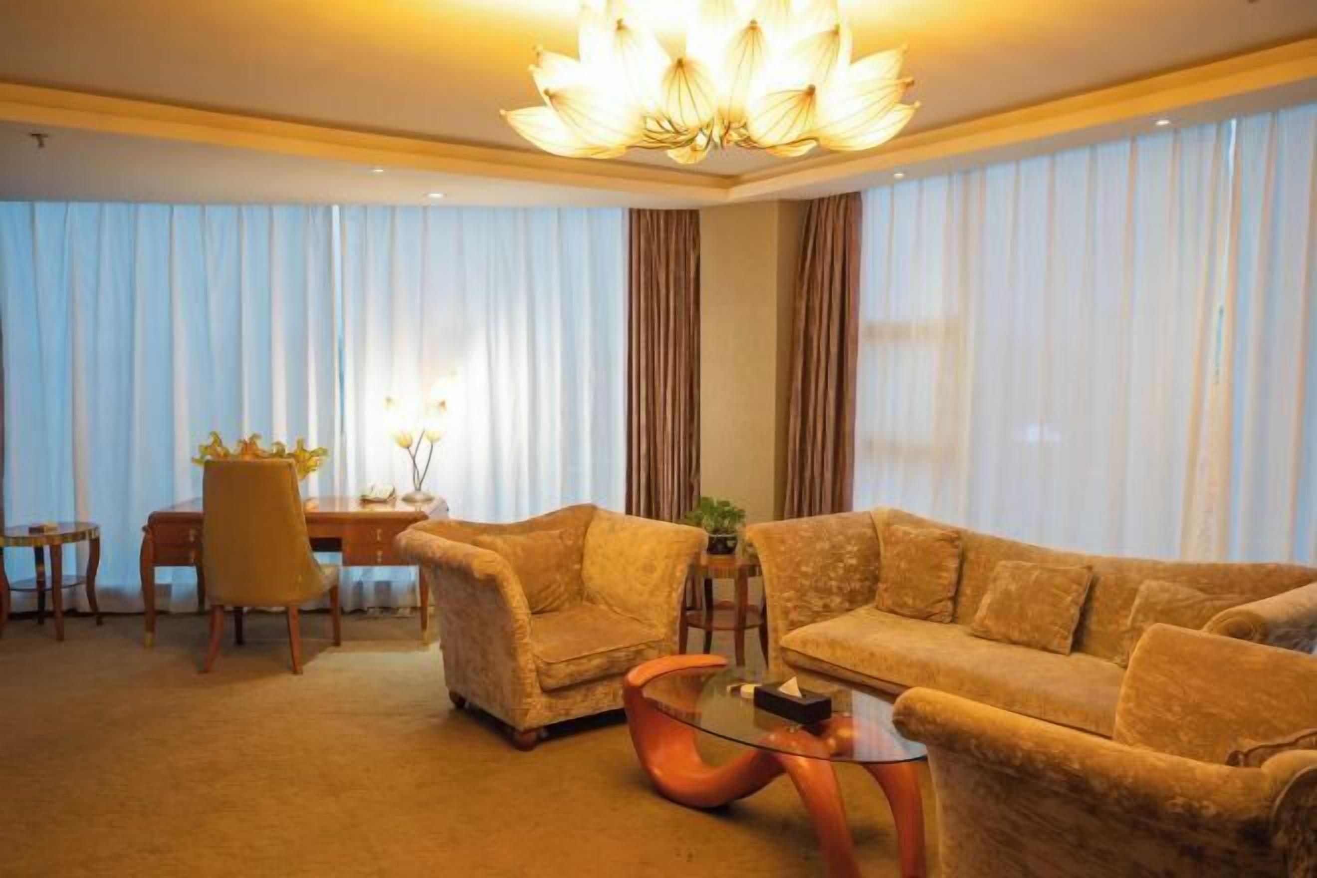 A hotel room with a large window, a sofa, a chair, a small table, and a decorative light fixture.