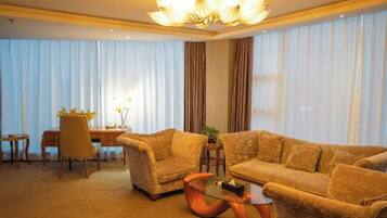 Habitación de hotel con un ventanal grande, un sofá, una silla, una mesita y una lámpara decorativa.