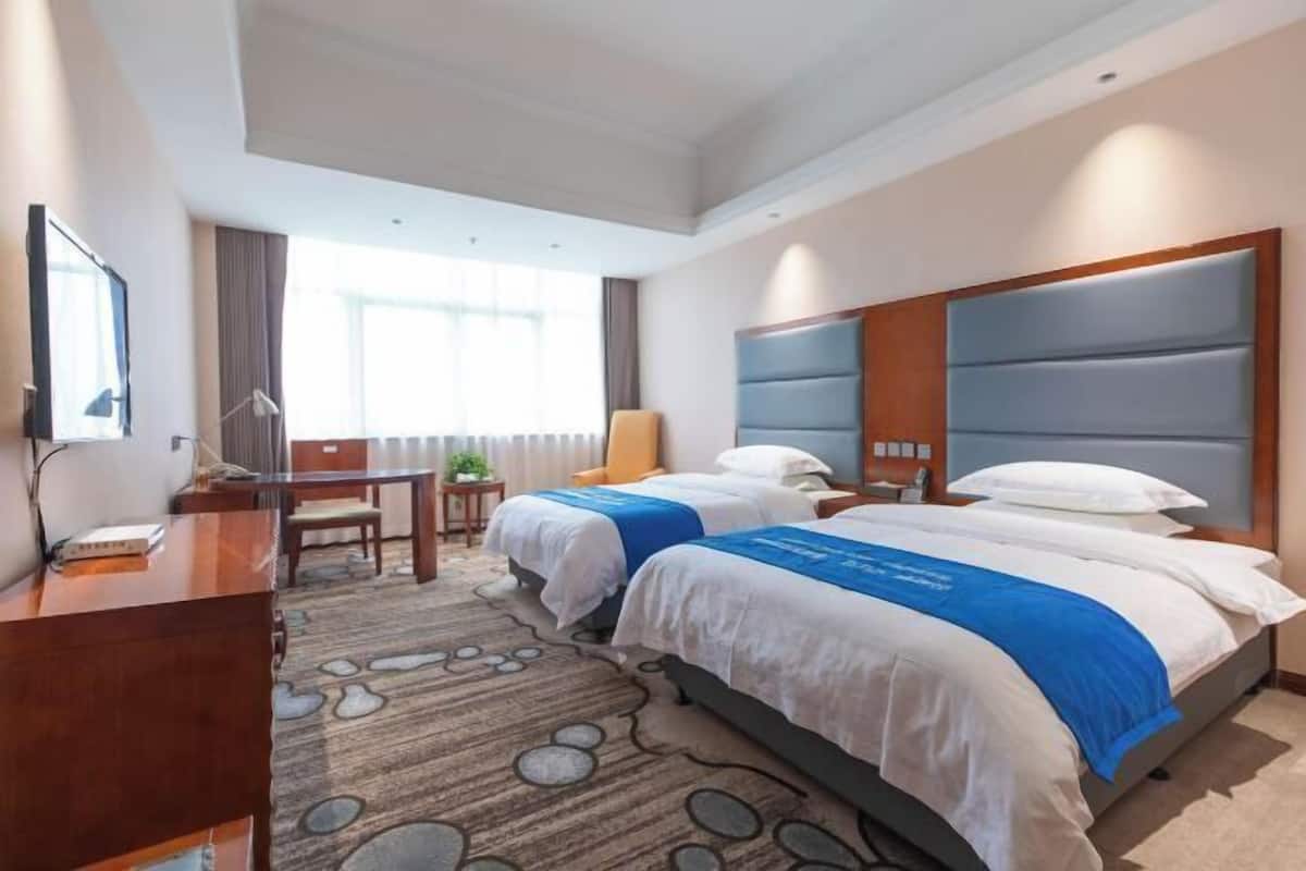 A hotel room with two beds, a desk, a chair, and a TV.