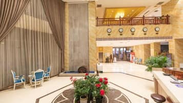 A hotel lobby with a reception desk, seating area, and a decorative plant centerpiece.