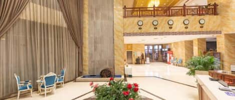 Un hall de hotel con mostrador de recepción, zona de estar y un centro de mesa con planta decorativa.