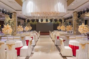 A banquet hall with rows of tables and chairs, a stage at the front, and floral decorations. - Dinis Hotel (Luoyang Kaiyuan) (Luoyang)