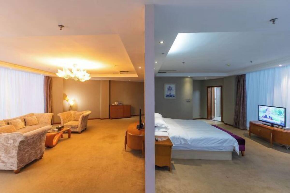 A hotel room with a sofa set, a bed, a television, and a desk.
