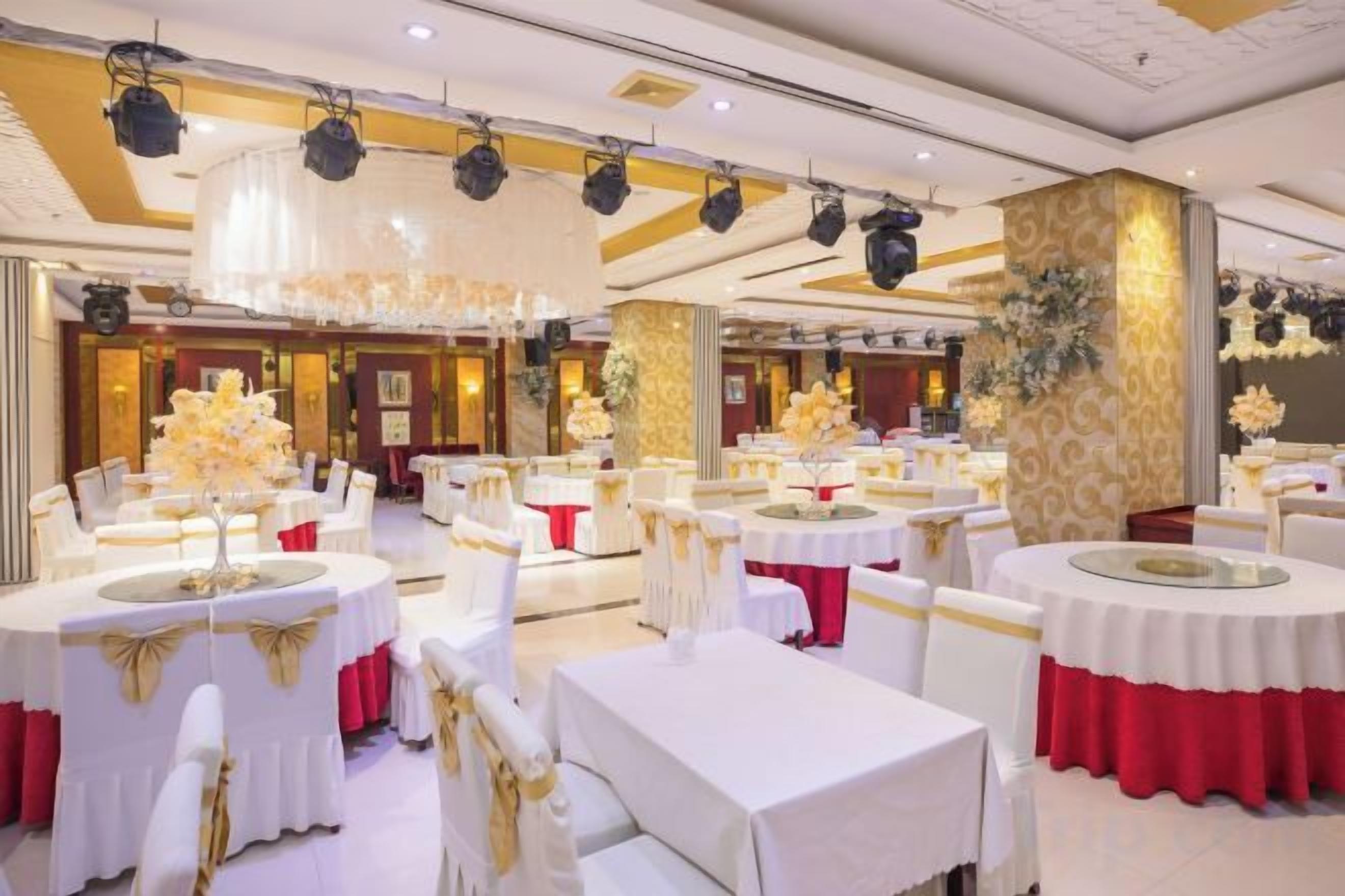 A banquet hall with round tables, white and red tablecloths, and gold accents.