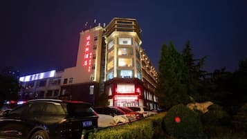 A hotel with a prominent red sign, multiple floors, and a parking lot with cars.