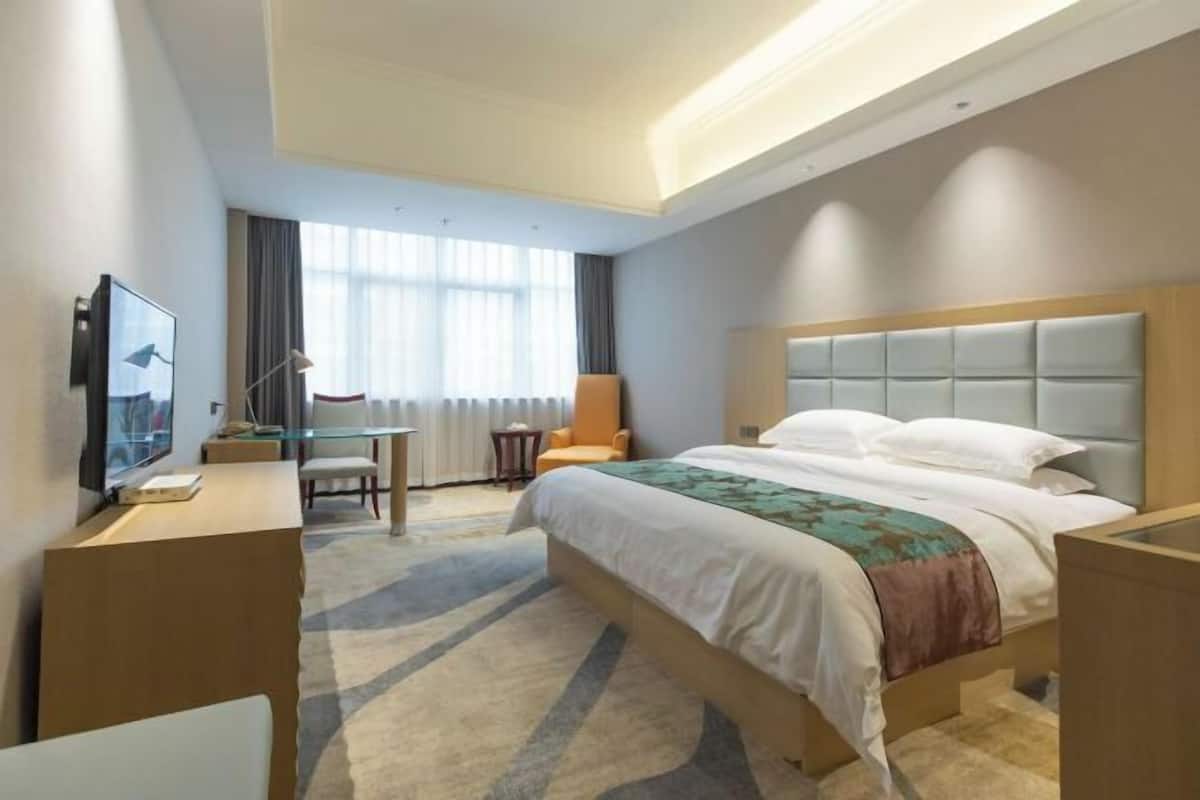 A hotel room with a bed, a desk with a computer, a chair, and a television.