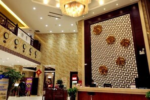 A hotel lobby with a reception desk, a decorative wall with geometric patterns, and a chandelier. - Dinis Hotel (Luoyang Kaiyuan) (Luoyang)