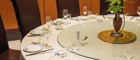 A round dining table with a glass top, surrounded by brown leather chairs, set with plates, cutlery, and glasses.