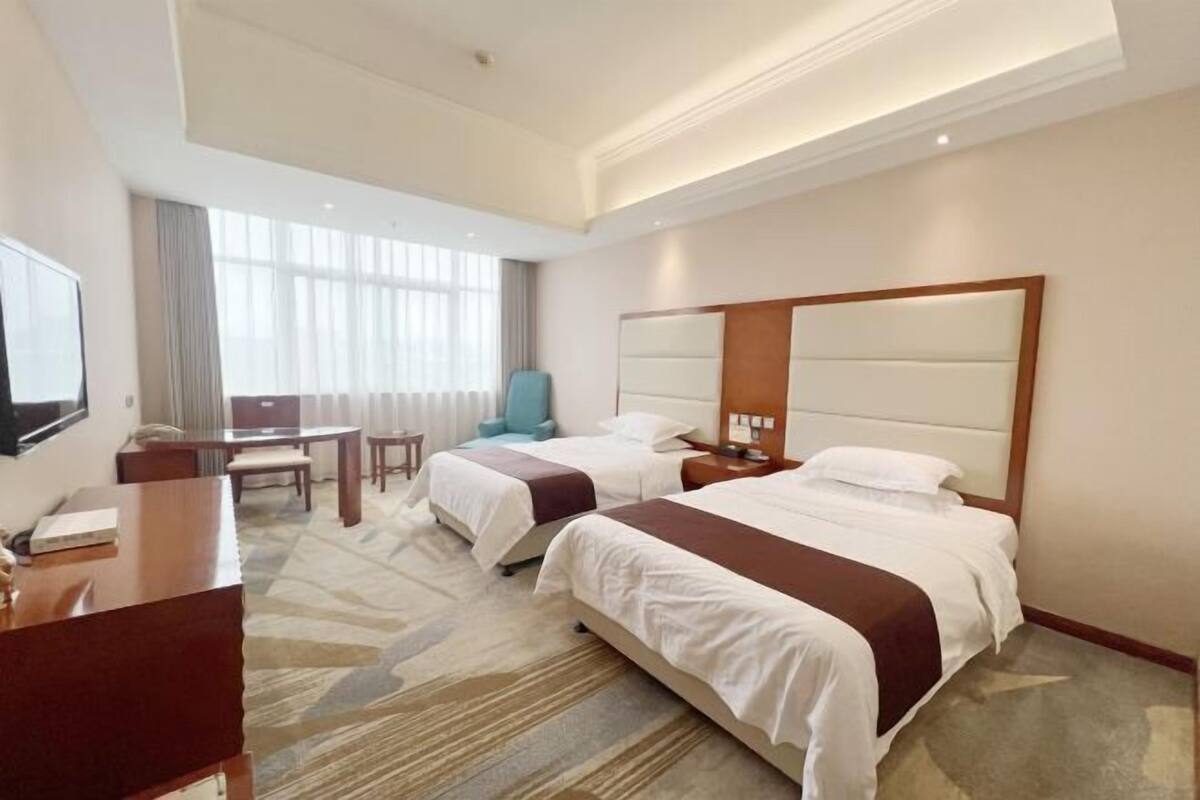 A hotel room with two beds, a desk, a chair, and a large mirror.