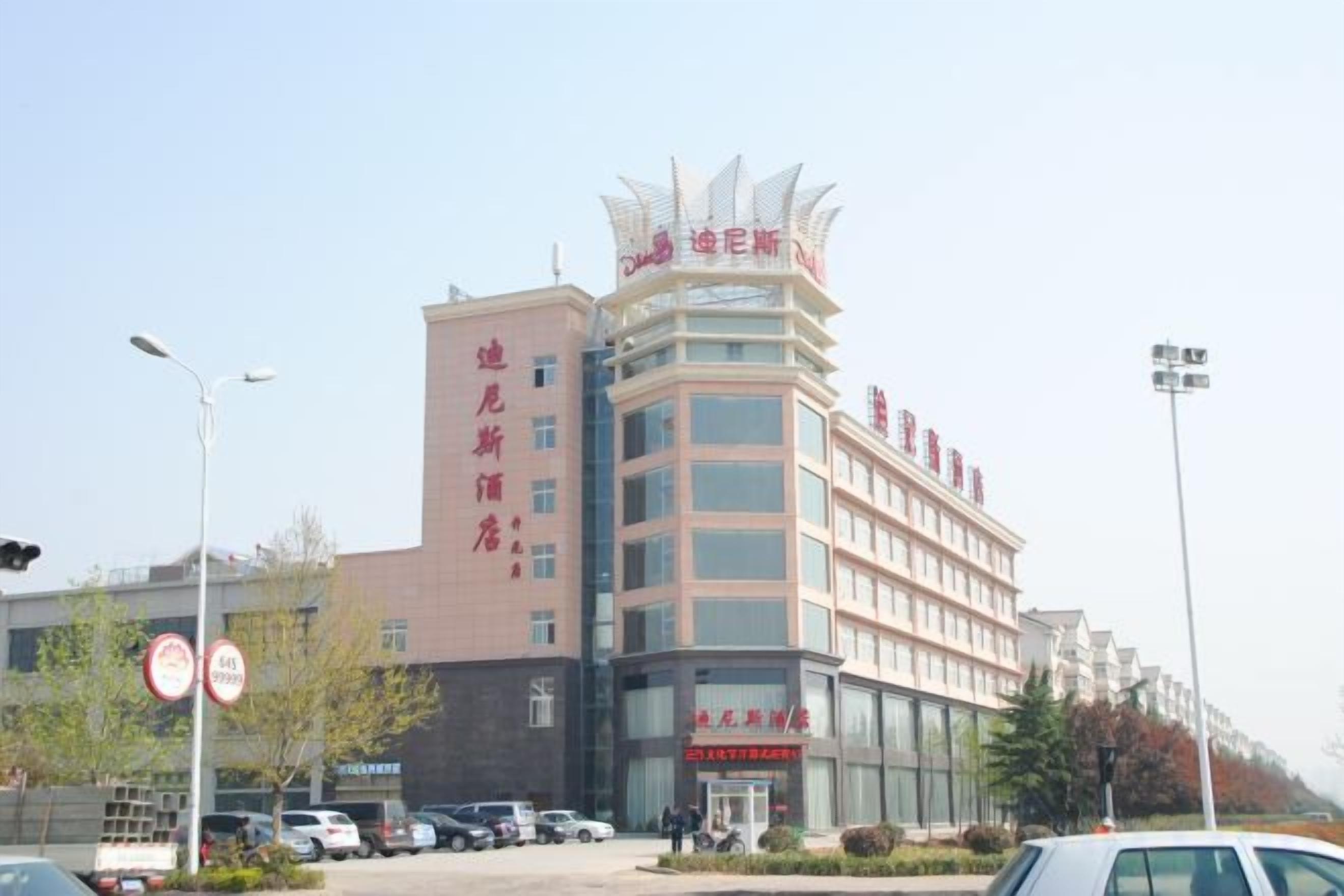 A multi-story hotel with a prominent sign at the top, a parking lot in front, and a clear sky.