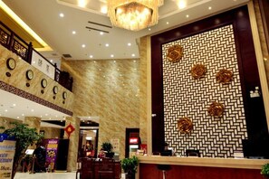 Un vestíbulo de hotel con mostrador de recepción, una araña y una escalera, además de un muro con diseño.