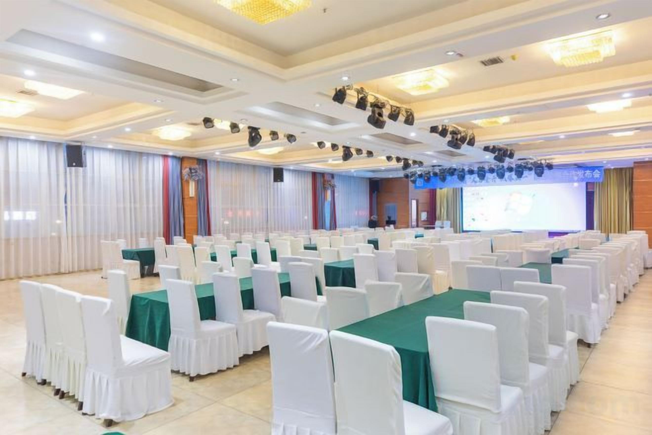 A conference room with rows of white chairs, a stage with a screen, and a chandelier.