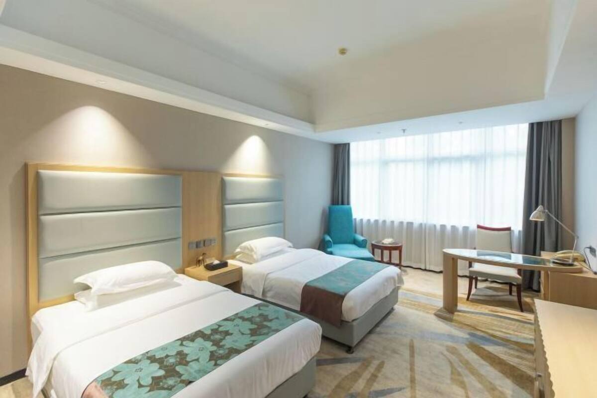 A hotel room with two beds, a desk, a chair, and a view of the outdoors.