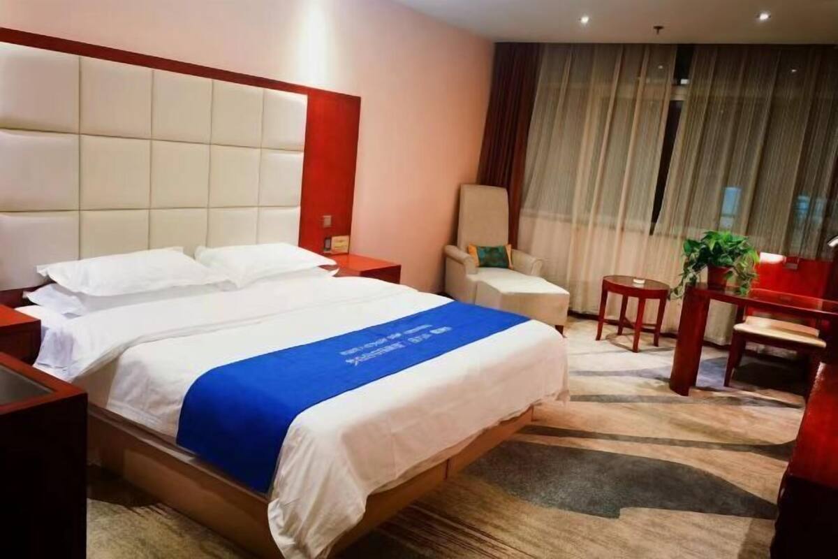 A hotel room with a large bed, a desk, a chair, and a small table.