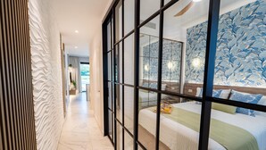 A hotel room with a large bed, a view through a glass partition, and a patterned wall.