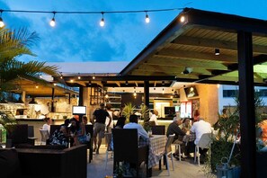 An outdoor dining area with tables and chairs, a covered seating area, and a bar with a stone counter. - Aqua Luxe @ Cana Rock terrace to pool access E-105 (Bavaro)