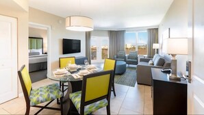 A modern hotel room with a dining area, a living area with a sofa and armchairs, a TV, and a view of the city. - July 4 week '25 close to Disney Kissimmee / Orlando (Kissimmee)