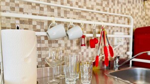 Una cocina con salpicadero de azulejos, un lavamanos de acero inoxidable y varios utensilios de cocina colgados en un colgador.