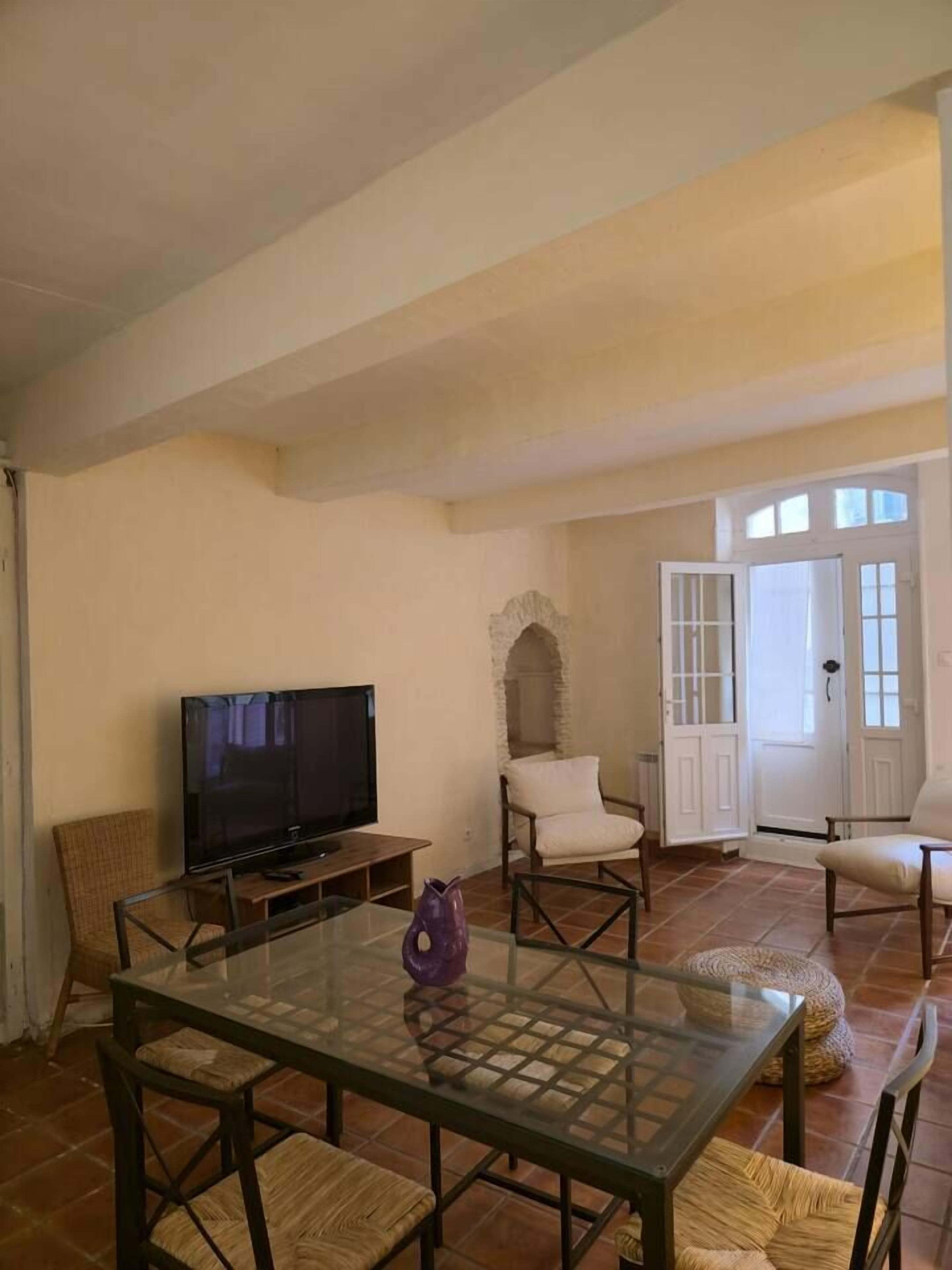 A spacious living room with a glass-top table, a television, and two chairs.