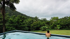 Een zwembad met uitzicht op weelderige begroeiing en een heuvel op de achtergrond.