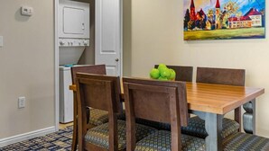 A dining area with a wooden table and chairs, a painting on the wall, and a white appliance in the background. - Charming 2-bedroom resort in lovely Midway with gym, indoor pool and more. (Midway)