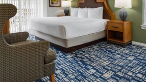A hotel room with a large bed, two bedside tables with lamps, a wooden headboard, a patterned carpet, and a chair. - Charming 2-bedroom resort in lovely Midway with gym, indoor pool and more. (Midway)